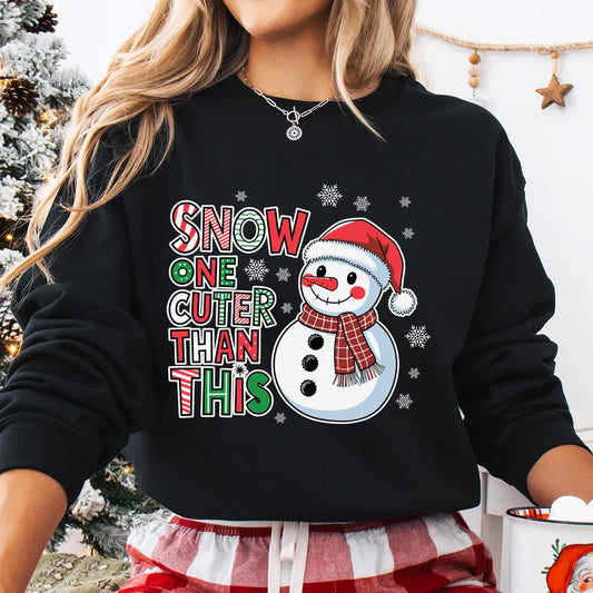 Black sweatshirt featuring a smiling snowman in a Santa hat and plaid scarf with the phrase “Snow One Cuter Than This” in festive red, green, and white lettering.