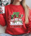Red sweatshirt featuring three smiling snowmen with scarves and hats and the phrase “Stay Groovy & Bright” in festive red and green lettering, ideal for Christmas apparel.