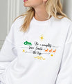 White sweatshirt featuring the phrase “Be Naughty, Save Santa the Trip” in elegant script with green sleigh, orange reindeer, and gold stars—funny minimalist Christmas design.