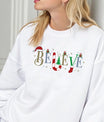 White sweatshirt featuring the word “BELIEVE” decorated with Santa hat, candy cane, Christmas tree, gifts, and stocking—classic festive DTF transfer design.