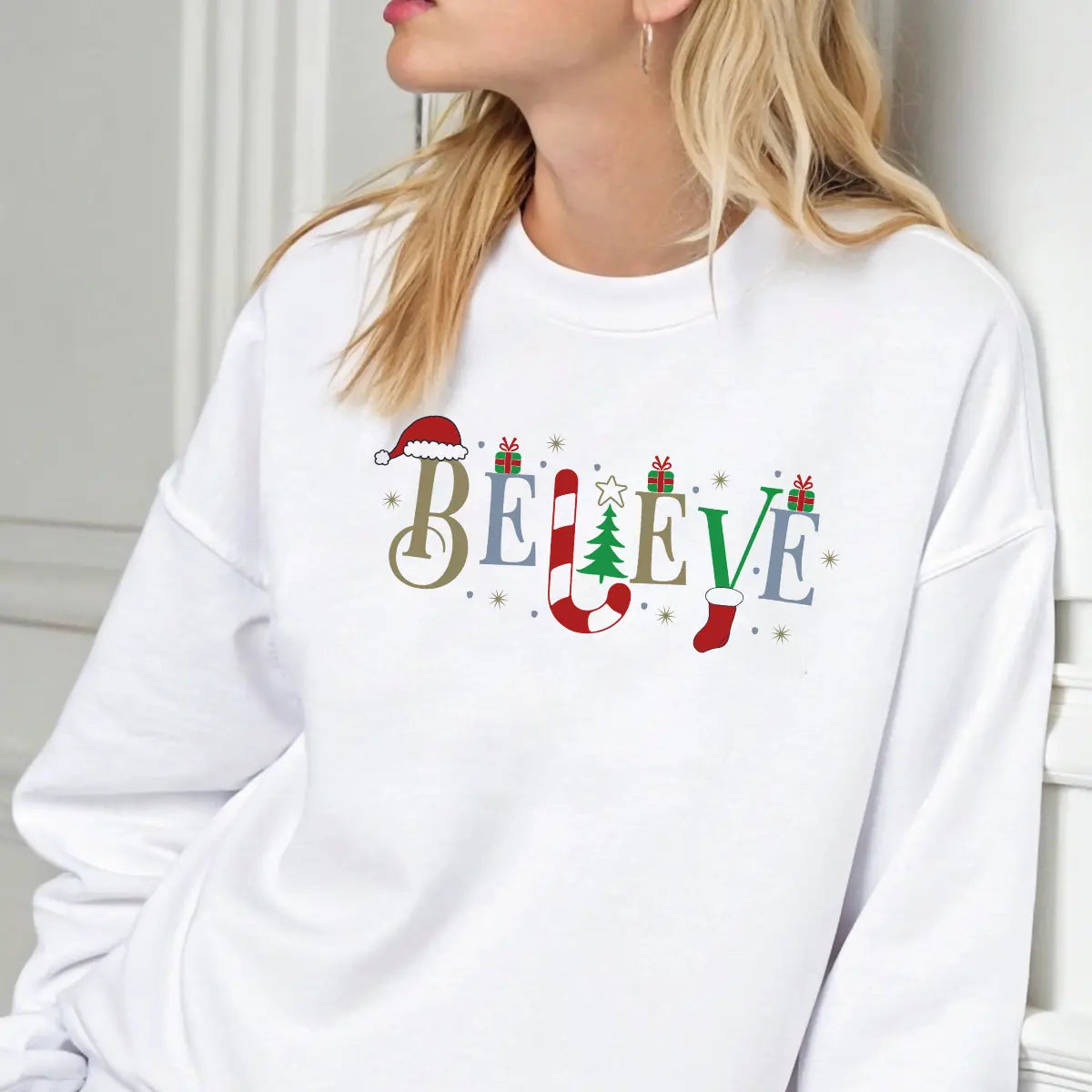White sweatshirt featuring the word “BELIEVE” decorated with Santa hat, candy cane, Christmas tree, gifts, and stocking—classic festive DTF transfer design.