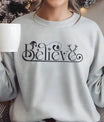 Gray sweatshirt featuring an elegant black script “Believe” design with Santa hat, ornament, snowflake, and antlers—minimal and festive Christmas DTF transfer.