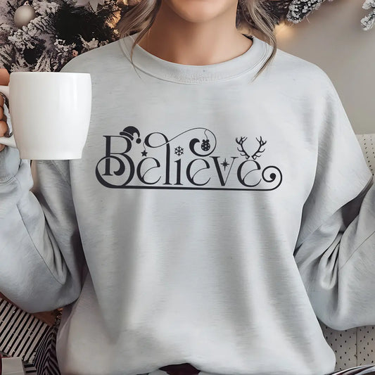 Gray sweatshirt featuring an elegant black script “Believe” design with Santa hat, ornament, snowflake, and antlers—minimal and festive Christmas DTF transfer.