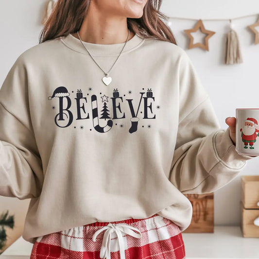 Beige sweatshirt featuring a black “Believe” DTF design with Santa hat, candy cane, Christmas tree, and gift accents—classic and elegant holiday apparel.