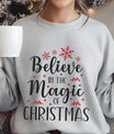 Gray sweatshirt featuring the phrase “Believe in the Magic of Christmas” in elegant black script with red snowflakes and accents—perfect for festive holiday apparel.