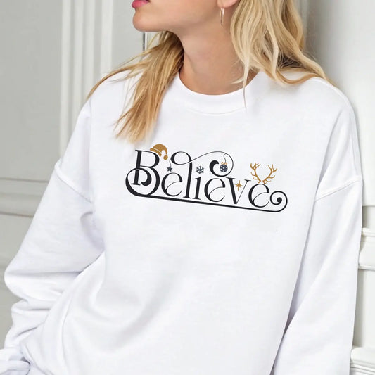 White sweatshirt featuring a black and gold “Believe” DTF design with Santa hat, ornament, and reindeer antlers—minimal and elegant Christmas style.