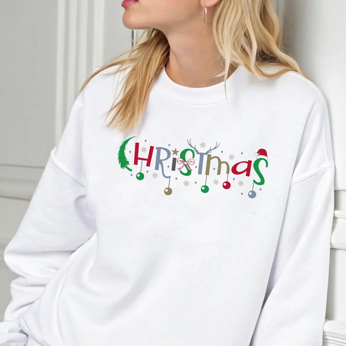 White sweatshirt with colorful “Christmas” DTF design featuring ornaments, stars, antlers, and Santa hat accents.