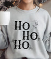 Gray sweatshirt with “Ho Ho Ho” Gothic-style DTF design featuring black letters, holly leaves, candy cane, and skull accents.