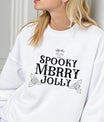 White sweatshirt with “Spooky Merry Jolly” Gothic Christmas DTF design featuring skull and holly leaf accents.