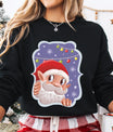 Black sweatshirt with a cute cartoon Santa peeking out against a snowy purple background with colorful lights.