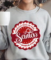 Gray sweatshirt with a red and white circular “Official Santa Seal of the North Pole” DTF transfer design featuring Santa’s hat.