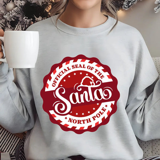 Gray sweatshirt with a red and white circular “Official Santa Seal of the North Pole” DTF transfer design featuring Santa’s hat.