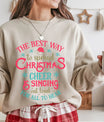 Sand-colored sweatshirt with red, teal, and gold “The Best Way to Spread Christmas Cheer” design featuring a Santa hat and snowflakes.