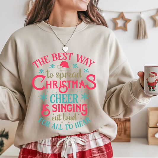 Sand-colored sweatshirt with red, teal, and gold “The Best Way to Spread Christmas Cheer” design featuring a Santa hat and snowflakes.