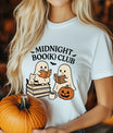 White t-shirt featuring two cute ghosts reading books with a cat, pumpkin, and coffee mug under text “Midnight Boo(k) Club.”