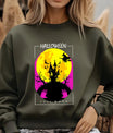 Green sweatshirt featuring a haunted house, witch, bats, and full moon Halloween DTF transfer design with bright yellow and pink tones.