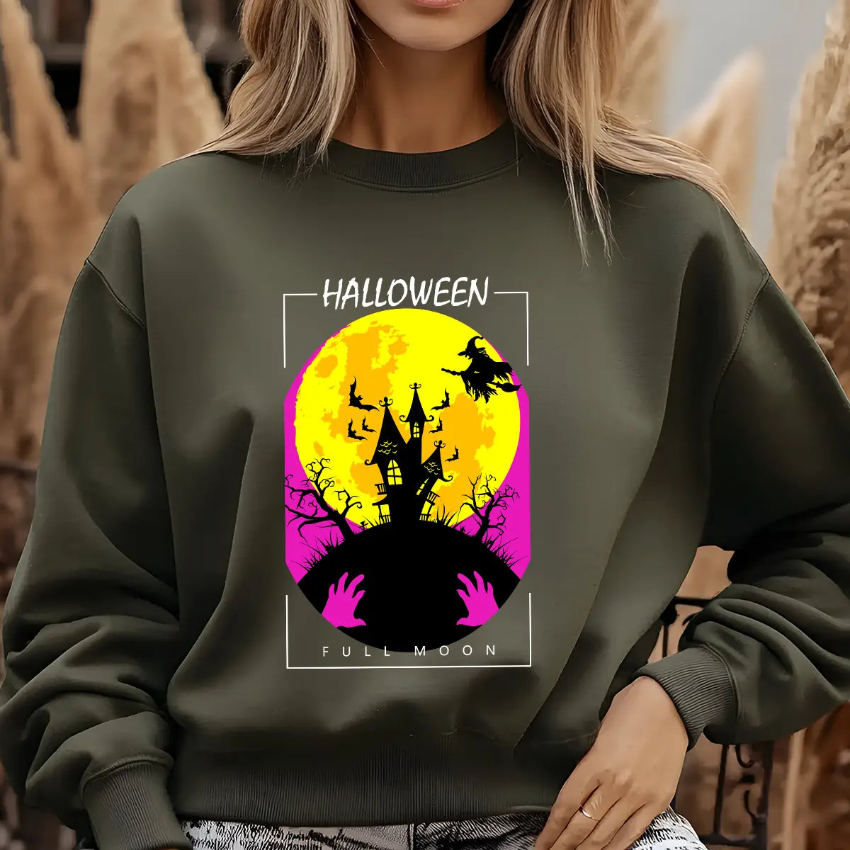 Green sweatshirt featuring a haunted house, witch, bats, and full moon Halloween DTF transfer design with bright yellow and pink tones.