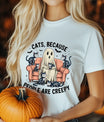 White t-shirt with “Cats Because People Are Creepy” DTF transfer featuring a ghost sitting on a couch surrounded by cute skeleton cats in a Halloween theme.