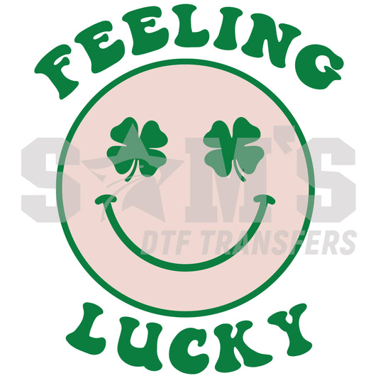 Graphic design with 'FEELING LUCKY' text in a green arc over a smiling face with two shamrock eyes, on a soft pink circle background.