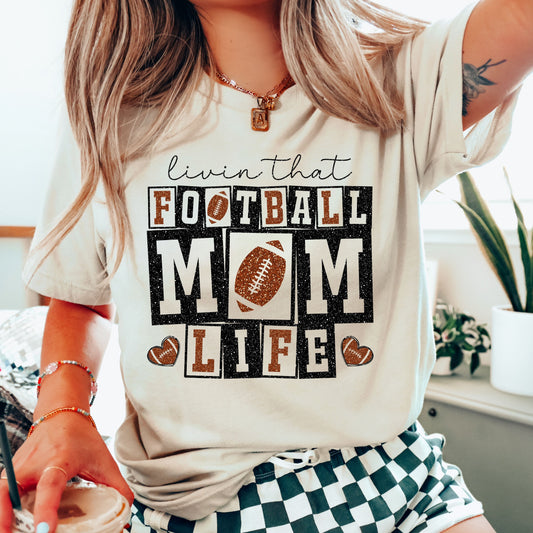 Livin’ That Football Mom Life DTF Transfer design on a beige t-shirt featuring glittery text and football graphics.