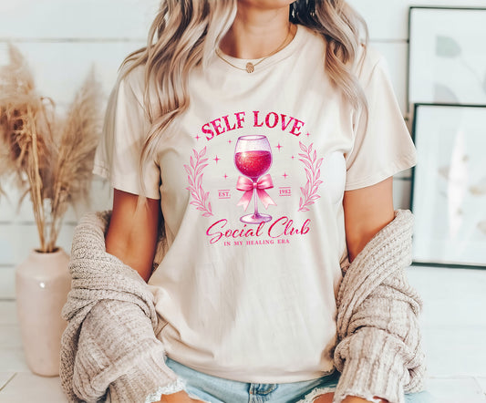 Self Love Social Club DTF Transfer design with a wine glass and pink accents on a cream T-shirt worn by a woman.