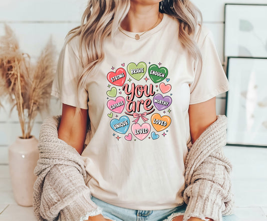 You Are Strong and Loved DTF transfer design with colorful affirmation hearts on a cream T-shirt.