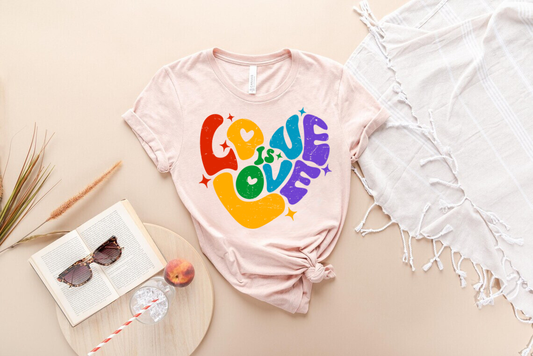 Love is Love Rainbow Heart DTF Transfer design on a light pink T-shirt styled with accessories.