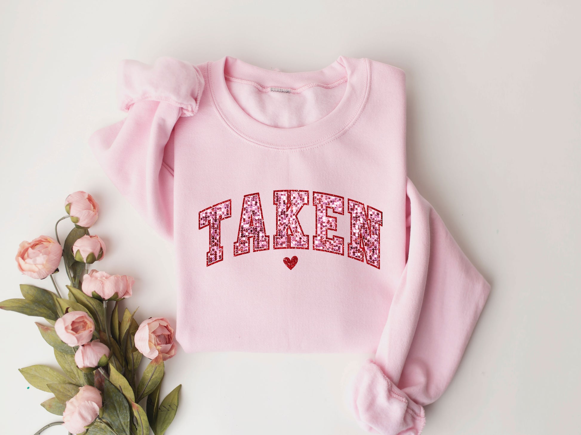 TAKEN Valentine's Day ready-to-press DTF Transfer design with glittery red letters and a heart on a pink sweatshirt.